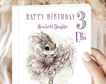 May include: A birthday card with a watercolor illustration of a bunny ballerina in a pink tutu. The card reads "Happy Birthday 3 Wonderful Daughter Ella" in purple script. The bunny is wearing a floral crown and ballet shoes.