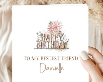 May include: A square white greeting card featuring the text HAPPY BIRTHDAY in a stylized font with pink and gold accents, topped with watercolor-style pink stars. Below, the text reads TO MY BESTEST FRIEND and the name Danielle in gold script.