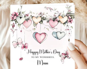 May include: A Mother's Day card with a watercolor design. The card features hanging hearts in shades of pink, peach, and white, adorned with floral accents. The text reads "Happy Mother's Day To My Wonderful Mum."
