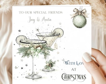 May include: A square greeting card featuring two martini glasses garnished with pine sprigs, pinecones, and bows. The text reads TO OUR SPECIAL FRIENDS Jay & Anita, and WITH LOVE AT CHRISTMAS. A pale green Christmas ornament hangs in the top right corner.