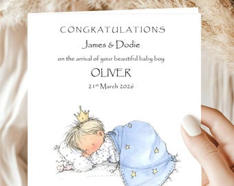 May include: A baby announcement card with the text "CONGRATULATIONS James & Dodie on the arrival of your beautiful baby boy OLIVER 21st March 2026." The illustration shows a sleeping baby wearing a crown and covered with a blue blanket.
