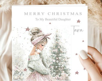 May include: A square Christmas greeting card featuring the text MERRY CHRISTMAS To My Beautiful Daughter and the name Tara. The illustration depicts a person with a high bun and headband, wearing a white sweater and pink skirt near a Christmas tree.