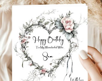 May include: A white greeting card with a floral heart-shaped wreath design. The card features a pink rose and the text "Happy Birthday To My Wonderful Wife Sam With Love."