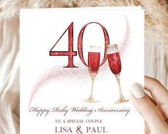 May include: A square greeting card with a white background featuring a large red glittery number 40, two champagne flutes filled with red liquid, and the text Happy Ruby Wedding Anniversary to a special couple Lisa & Paul in red font.