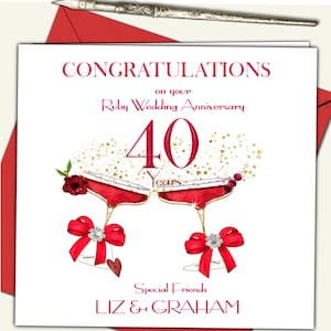 May include: A white card with red and gold text and illustrations. The card says "Congratulations on your Ruby Wedding Anniversary 40 Years". It features two red wine glasses with red bows and a red rose. The card is signed "Special Friends Liz & Graham".