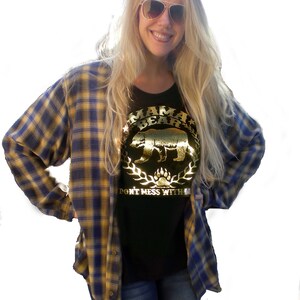 Puede incluir: Una camiseta negra con un dise&ntilde;o en l&aacute;mina dorada que dice "Mama Bear" con una silueta de oso y las palabras "Don't Mess With" debajo.