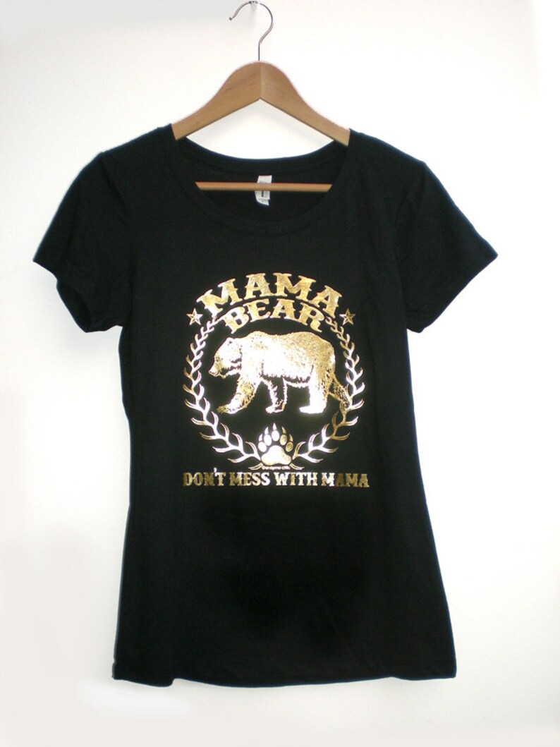 Puede incluir: Camiseta negra con un dise&ntilde;o de oso en oro en relieve dentro de una corona con el texto "Mama Bear" y "Don't Mess With Mama".