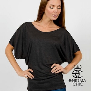 Pu&ograve; includere: Una maglietta grigia scura, larga, a maniche corte e scollo rotondo. La maglietta &egrave; realizzata in un tessuto morbido e confortevole e ha una vestibilit&agrave; rilassata. La modella indossa la maglietta con jeans blu.