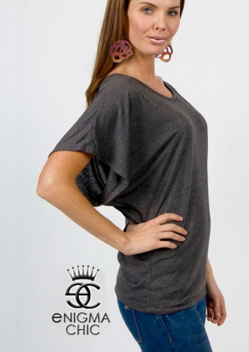Pu&ograve; includere: Una maglia grigia antracite, ampia, a maniche corte e con scollo rotondo. La maglia &egrave; realizzata in un tessuto morbido e confortevole. La modella indossa la maglia con jeans blu.