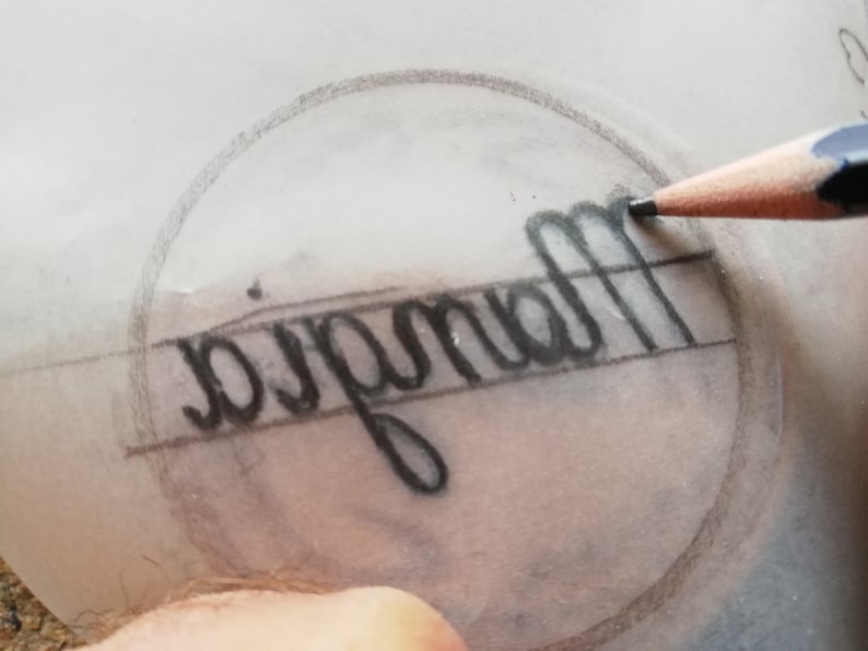 May include: A close-up of a pencil drawing on a piece of tracing paper. The drawing is of the word "Magnolia" inside a circle.