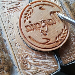May include: A close-up of a wooden stamp with the word "Duomo" carved into it. The stamp is being carved with a small knife.