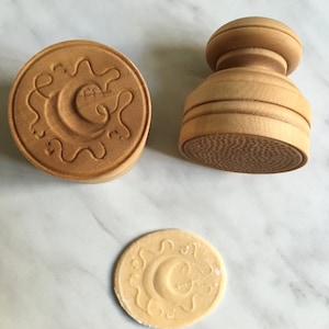 May include: Two wooden cookie cutters, one with a circular design and the other with a textured surface, and a cookie with the same design as the circular cutter.