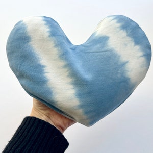 Pode incluir: Uma almofada em forma de cora&ccedil;&atilde;o com estampa tie-dye em tons de azul e branco. A almofada &eacute; feita de tecido macio e tem um padr&atilde;o tie-dye sutil.
