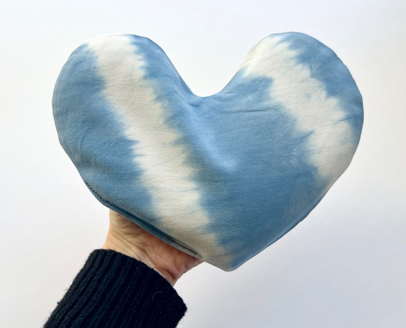 Pode incluir: Uma almofada em forma de cora&ccedil;&atilde;o com estampa tie-dye em tons de azul e branco. A almofada &eacute; feita de tecido macio e tem um padr&atilde;o tie-dye sutil.