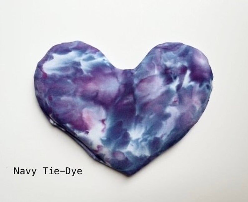 Puede incluir: Una almohada para los ojos con forma de coraz&oacute;n, te&ntilde;ida en azul marino, morado y blanco. La almohada est&aacute; hecha de tela suave y es perfecta para relajarse.