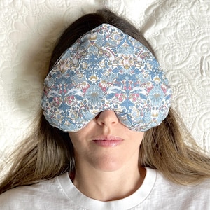 May include: A person wearing a blue and white floral eye mask while lying on a white bed.