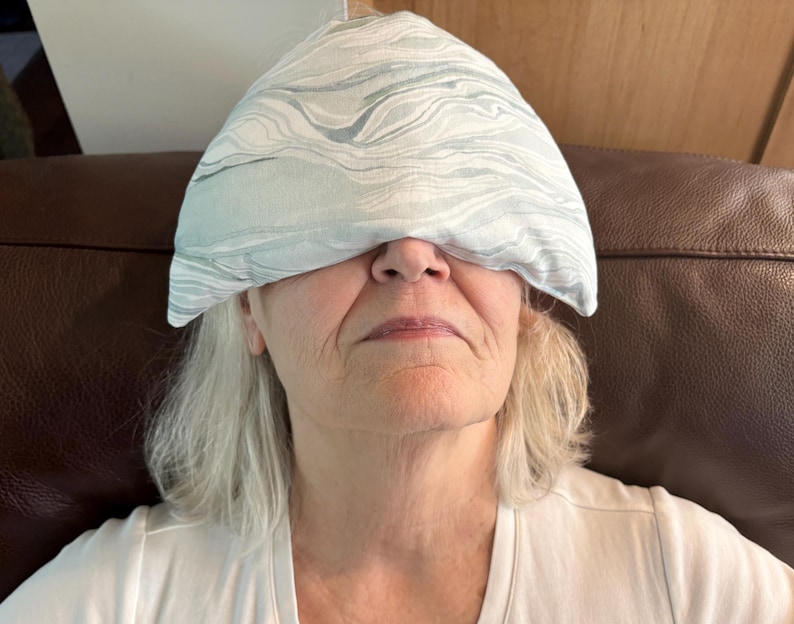 May include: A white eye mask with a blue and gray marbled pattern. The eye mask is placed over the eyes of a person lying on a brown leather couch.