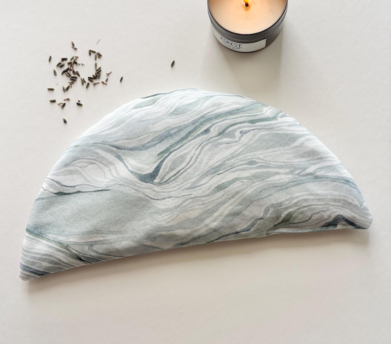 Puede incluir: Una almohadilla t&eacute;rmica de tela de color gris y blanco con un dise&ntilde;o de m&aacute;rmol en forma de media luna. La almohadilla est&aacute; hecha de tela suave y natural, ideal para aliviar dolores.