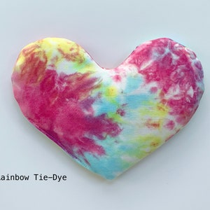 Puede incluir: Una almohada de coraz&oacute;n tie-dye con un patr&oacute;n de arco&iacute;ris en tonos de rosa, azul, amarillo y blanco. La almohada est&aacute; hecha de tela suave y tiene un brillo sutil.  Rainbow Tie-Dye