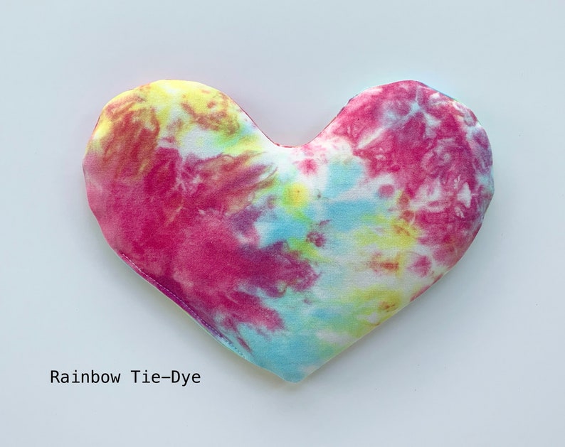 Puede incluir: Una almohada de coraz&oacute;n tie-dye con un patr&oacute;n de arco&iacute;ris en tonos de rosa, azul, amarillo y blanco. La almohada est&aacute; hecha de tela suave y tiene un brillo sutil.  Rainbow Tie-Dye
