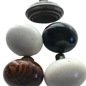 May include: A collection of five oval-shaped door knobs featuring varied finishes. The set includes two smooth white knobs, one glossy black knob, one brown and black marbled pattern knob, and one metallic grey knob with a visible mounting hole.