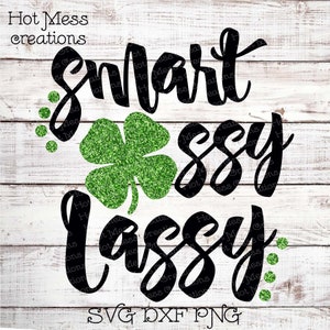 May include: Black and green SVG design with the text "Smart Sassy Lassie" and a green shamrock with glitter. The design is on a white wood background.