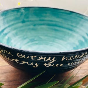 Peut inclure: Un bol en céramique avec un intérieur turquoise et un extérieur bleu foncé. Le bol porte une inscription manuscrite en blanc sur l'extérieur. Le bol est posé sur une surface en bois. C'est un objet décoratif.