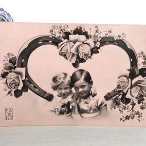 Antike französische Postkarte, hübsches Mädchen und Junge in einem Herz, Hufeisen und Rosen, Pastellrosa