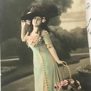 Antike Postkarte, hübsche Frau in großem Hut, die einen Korb mit rosa Blumen hält, handkolorierte Fotografie, Jugendstil