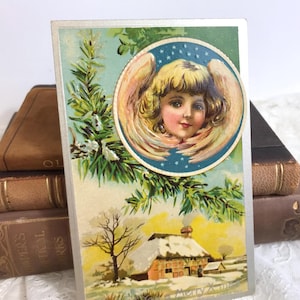 Antike Weihnachtspostkarte, Engel im Rahmen über schneebedeckten Häusern, Stark geprägt, Jugendstil