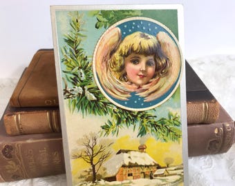 Antike Weihnachtspostkarte, Engel im Rahmen über schneebedeckten Häusern, Stark geprägt, Jugendstil