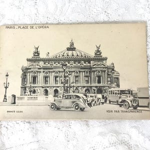 May include: A vintage black and white postcard featuring the Palais Garnier in Paris, labeled PARIS - PLACE DE L'OPÉRA, BREVETÉ S.G.D.G., and VOIR PAR TRANSPARENCE. The scene depicts the opera house with classic cars and a bus in the foreground.