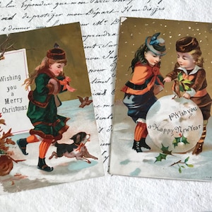 Zwei viktorianische Weihnachtskarten, Junge und Mädchen mit Schneeball, Mädchen und Welpe im Schnee, aus dem Album wiedergewonnen, 1880er Jahre