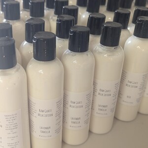 May include: A collection of white lotion bottles with black caps. Each bottle has a label that reads "Raw Goats Milk Lotion" and "Lavender Vanilla". The bottles are arranged closely together, suggesting a bulk product.