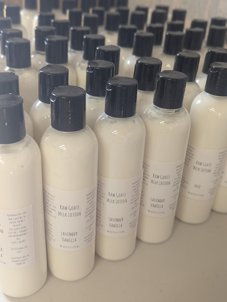 May include: A collection of white lotion bottles with black caps. Each bottle has a label that reads "Raw Goats Milk Lotion" and "Lavender Vanilla". The bottles are arranged closely together, suggesting a bulk product.