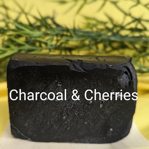 May include: A black bar of soap with the text "Charcoal & Cherries" printed on it. The soap is sitting on a white surface.