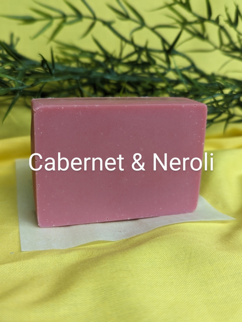 May include: A rectangular bar of soap with the text "Cabernet & Neroli" printed on the front. The soap is a light pink color and is sitting on a white piece of paper.