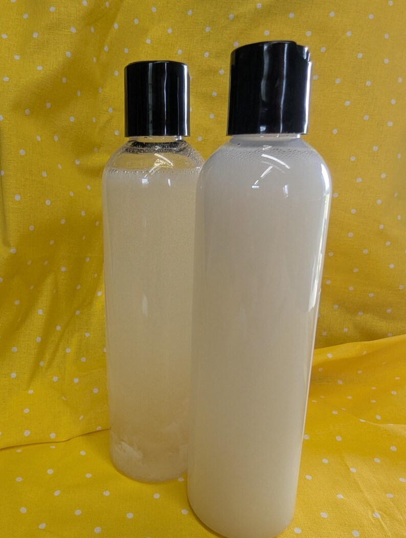 May include: Two clear plastic bottles filled with a light-colored liquid, each topped with a black cap. The bottles are cylindrical and appear to contain a cosmetic product, set against a yellow background with white polka dots.