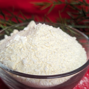 May include: A glass bowl filled with white, finely shredded coconut flakes. The bowl is sitting on a red surface.