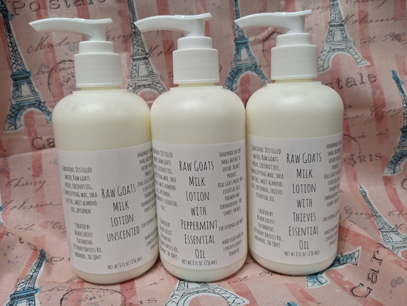 K&ouml;nnte beinhalten: Drei wei&szlig;e Lotionflaschen mit Pumpspendern. Jede Flasche hat ein Etikett mit der Aufschrift "Raw Goats Milk Lotion" mit verschiedenen &auml;therischen &Ouml;len. Die Flaschen stehen auf einem rosa Stoff mit Eiffelturm- und Postkartendesigns.