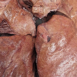 May include: Close-up of a pile of raw, brown beef liver. The liver is fresh and has a slightly wet, shiny surface.
