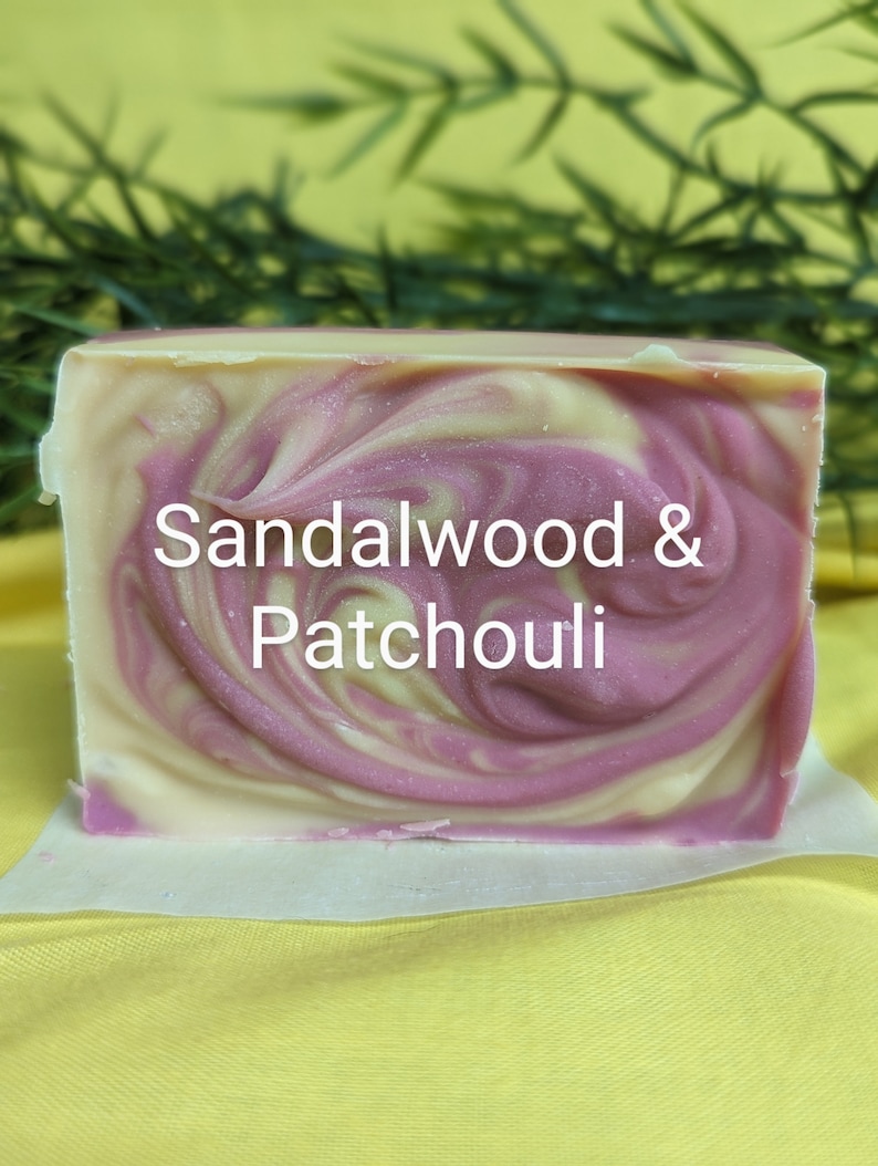 May include: A bar of handmade soap with a swirl design in shades of pink and white. The soap is labeled "Sandalwood & Patchouli".