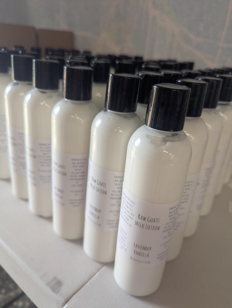 May include: A collection of white lotion bottles with black caps. Each bottle has a label that reads "Raw Goats Milk Lotion, Lavender Vanilla". The bottles are arranged on a white surface.