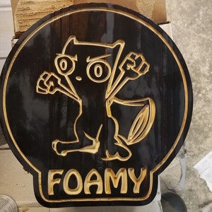 May include: A black wooden sign with a cartoon character and the word "FOAMY" carved into it. The character is a stylised animal with large eyes and raised fists.