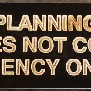 May include: A black sign with gold lettering that reads "Lack of planning on your part, does not constitute an emergency on my part."