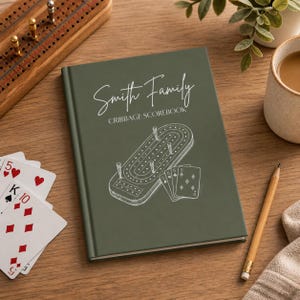 May include: A dark olive green hardback scorebook featuring white text reading Smith Family CRIBBAGE SCOREBOOK and a white line illustration of a cribbage board with pegs and playing cards positioned on the front cover.