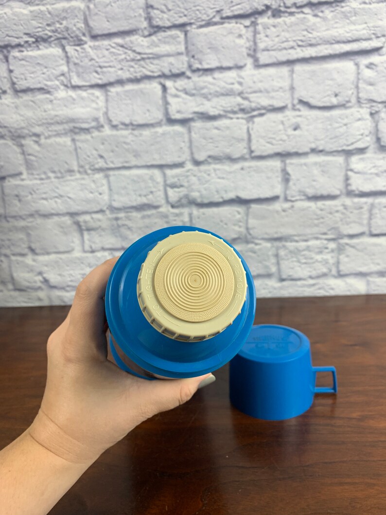 May include: Blue and white thermos with a lid and a matching cup. The thermos has a white lid with a circular design and the text "Thermos" on it.