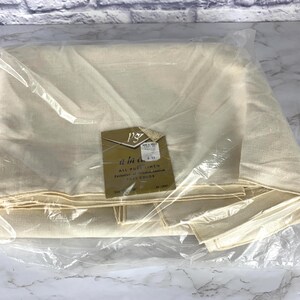 May include: A folded, cream-colored linen fabric is encased in a clear plastic bag. A small, tan tag with text is attached to the fabric. The tag reads "a la carte" and "All Pure Linen".