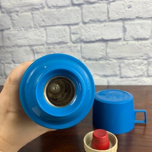 May include: Blue thermos with a red lid and a blue cup. The thermos has a silver opening for pouring.
