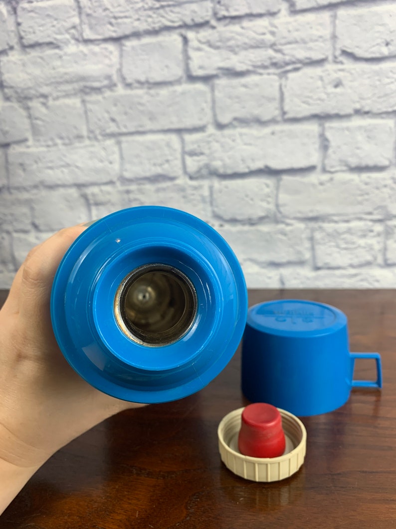 May include: Blue thermos with a red lid and a blue cup. The thermos has a silver opening for pouring.